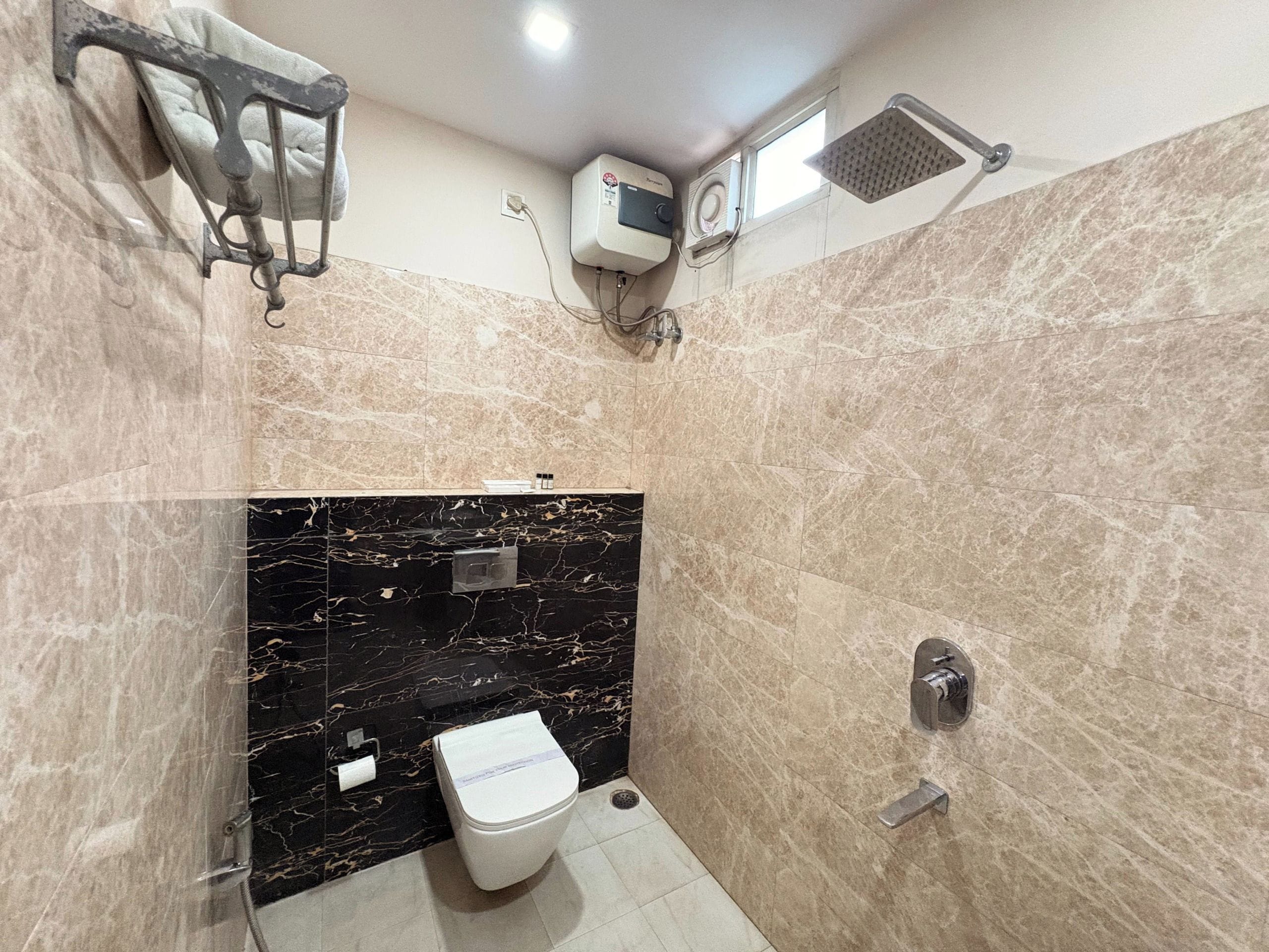 Une salle de bain équipée de toilettes, d’un porte-serviettes, d’une pomme de douche et d’un climatiseur fixé au mur.