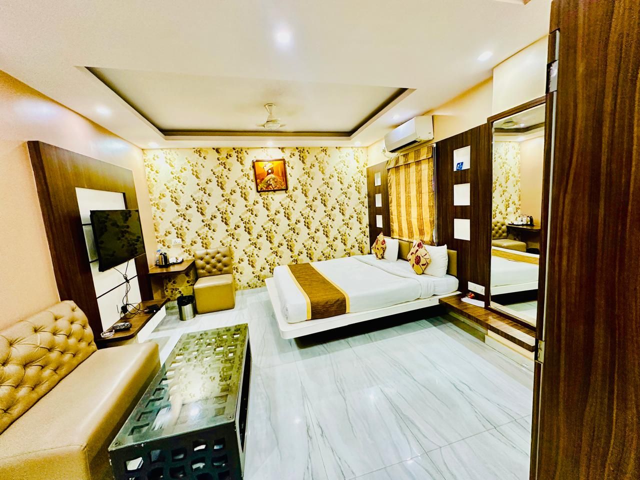 Une chambre d’hôtel avec un lit, un canapé, une table basse, une télévision et un miroir dans la salle de bain.