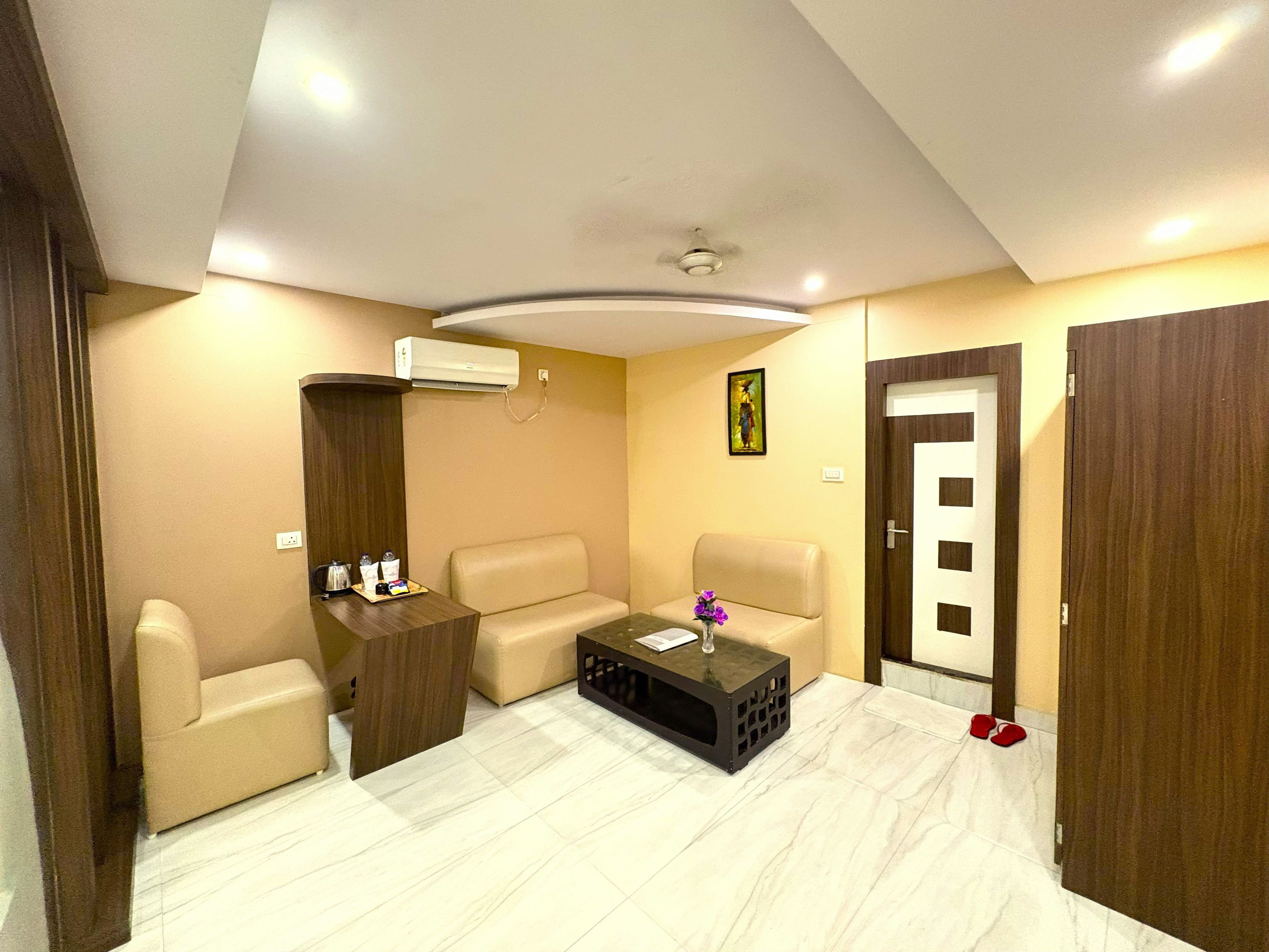 Una habitación de hotel con sofá, una mesa de centro, unidad de aire acondicionado y una puerta.