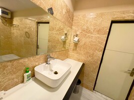 Un baño con lavamanos blanco, un espejo y pared de mármol.