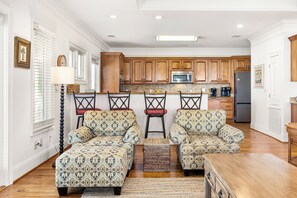 A spacious living room with a large sofa set and a dining area with a bar stool. - It's 5 O'Clock Somewhere! Ocean Views, Steps to the Beach by Tybee Cottages (Tybee Island)