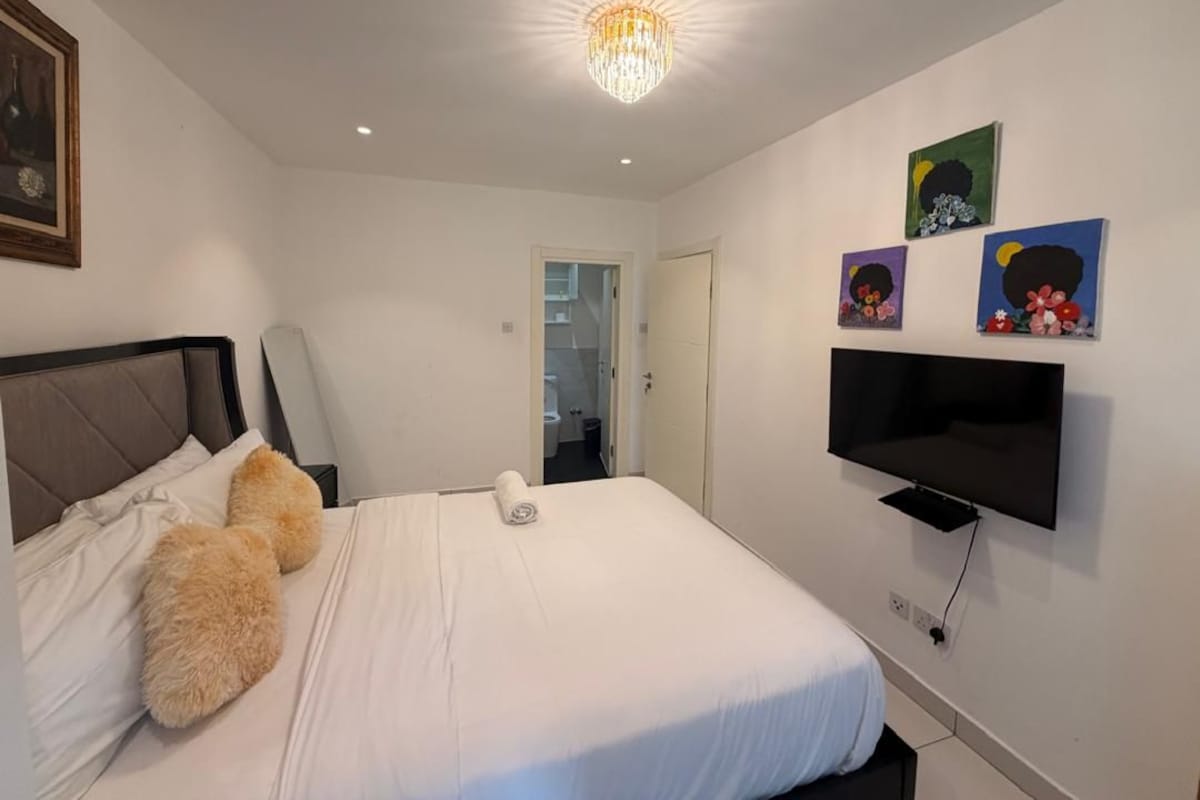 Un dormitorio con cama, televisor montado en la pared y obras de arte decorando la pared.