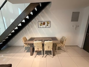 Un comedor con mesa y sillas, una escalera y un cuadro en la pared.