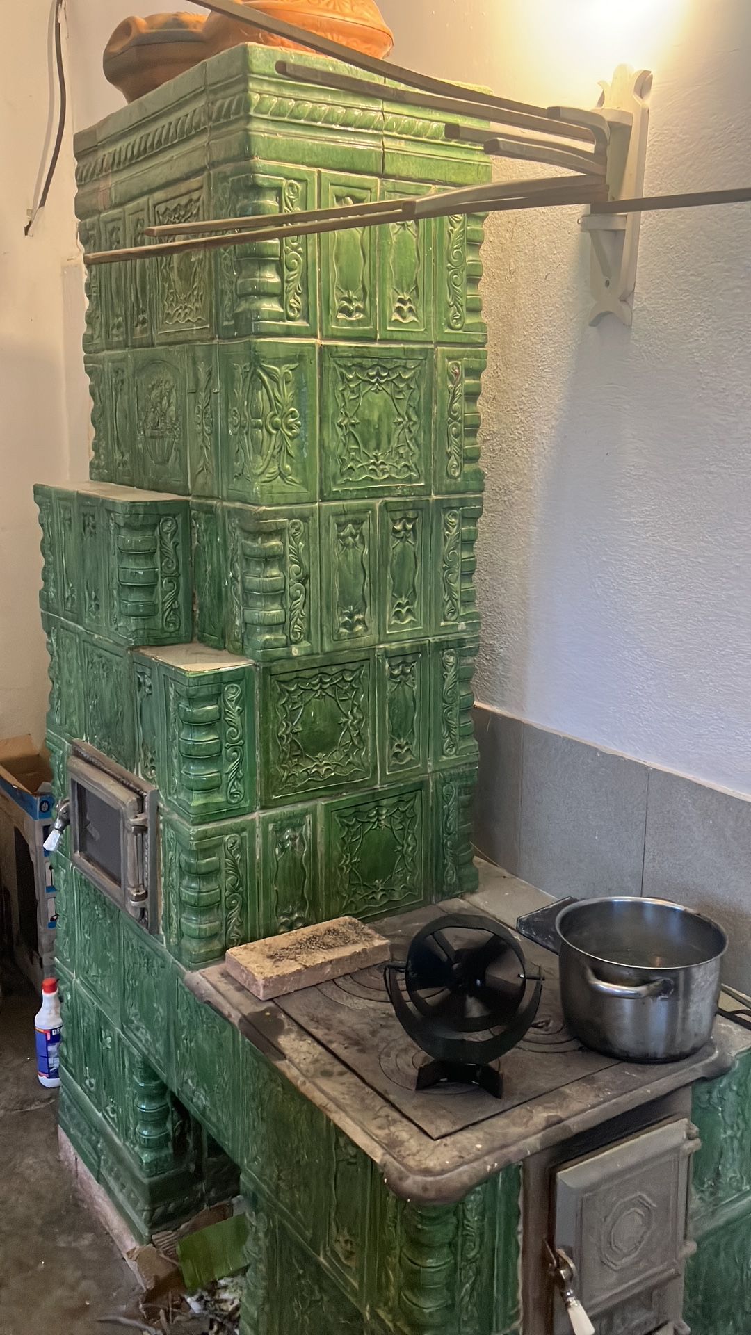 A green, ornate stove with a pot on top, a small window, and a metal container on the counter.