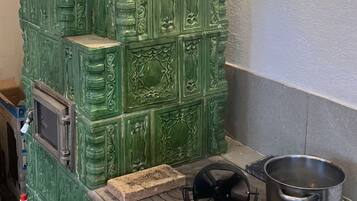 A green, ornate stove with a pot on top, a small window, and a metal container on the counter.