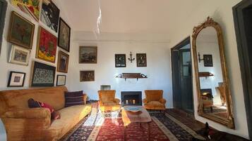 Una sala de estar con chimenea, un espejo grande y varias obras de arte enmarcadas en las paredes.