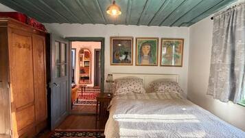 Un dormitorio con un armario de madera, una cama con colcha estampada, un tapete rojo y negro, y una lámpara en el techo.