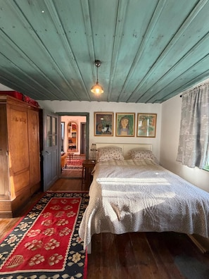 Et soveværelse med et træskab, en seng med et mønstret tæppe, en rød og sort måtte samt en lampe i loftet.