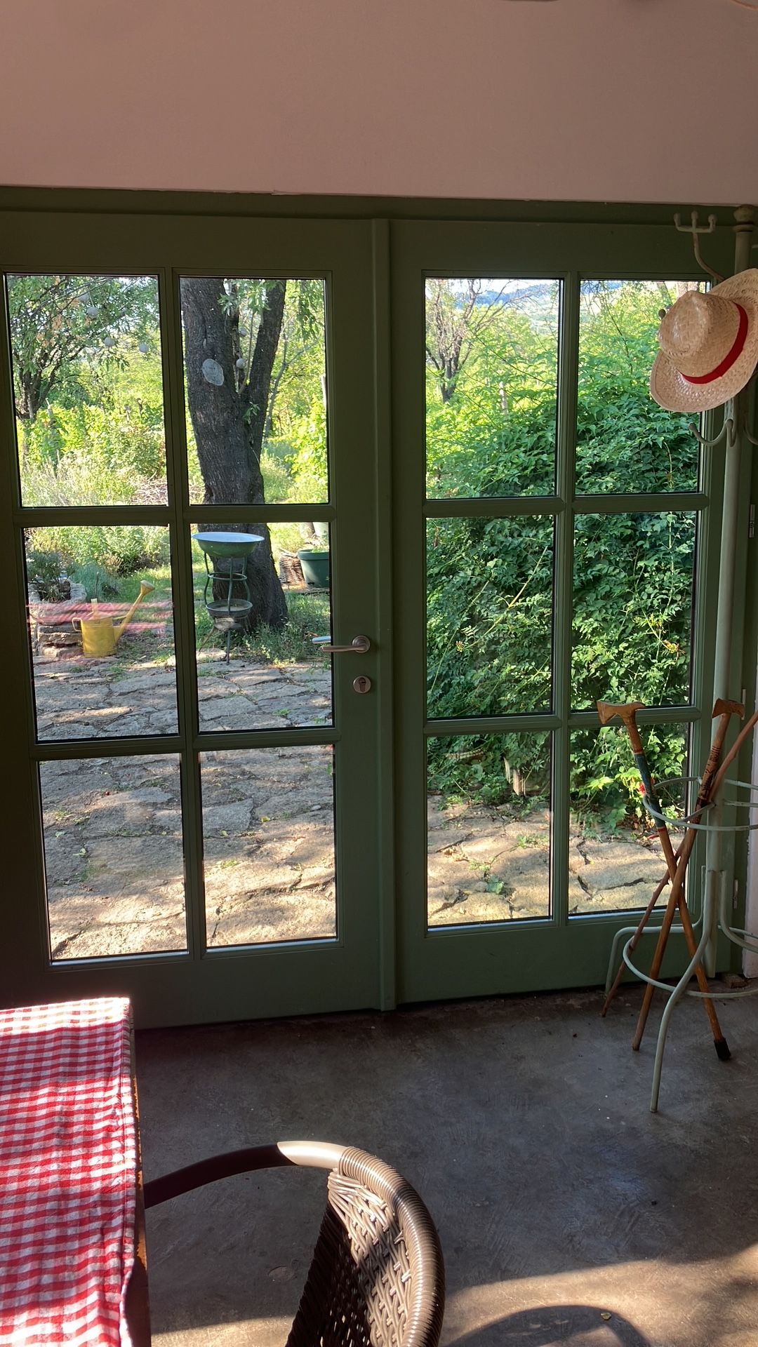 A room with a green door leading to an outdoor area with a tree, a wheelbarrow, and gardening tools.