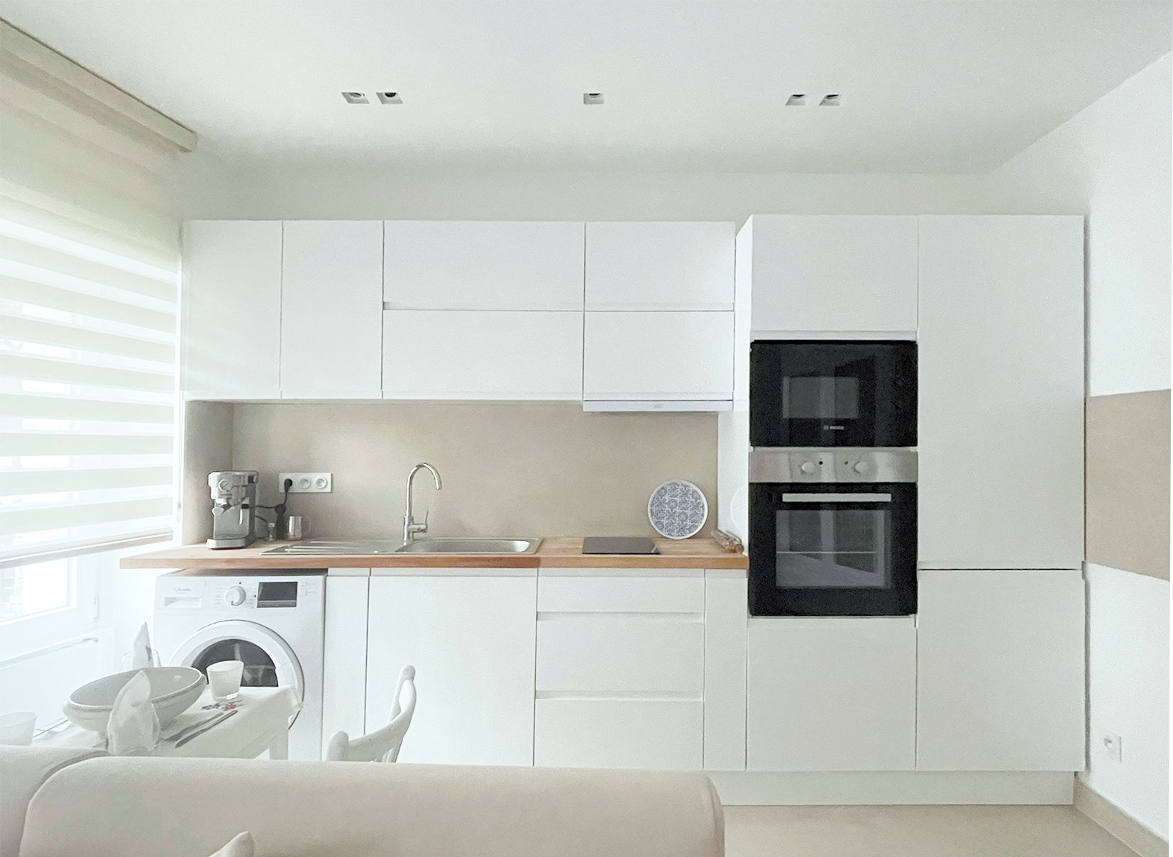 A modern kitchen with white cabinetry, a built-in oven, and a coffee maker.