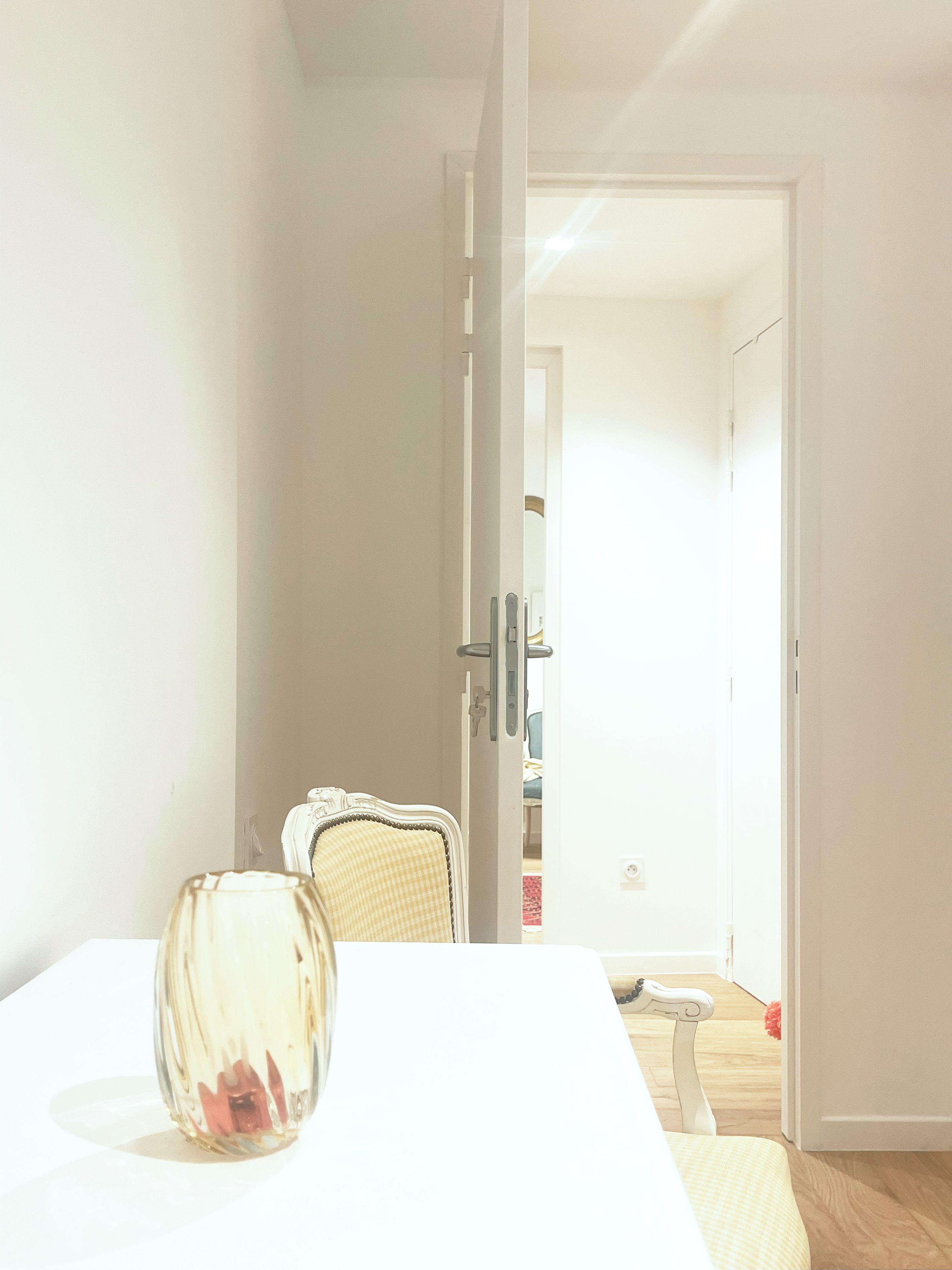 Una habitación con una mesa blanca, una silla y una puerta que da a otra estancia.