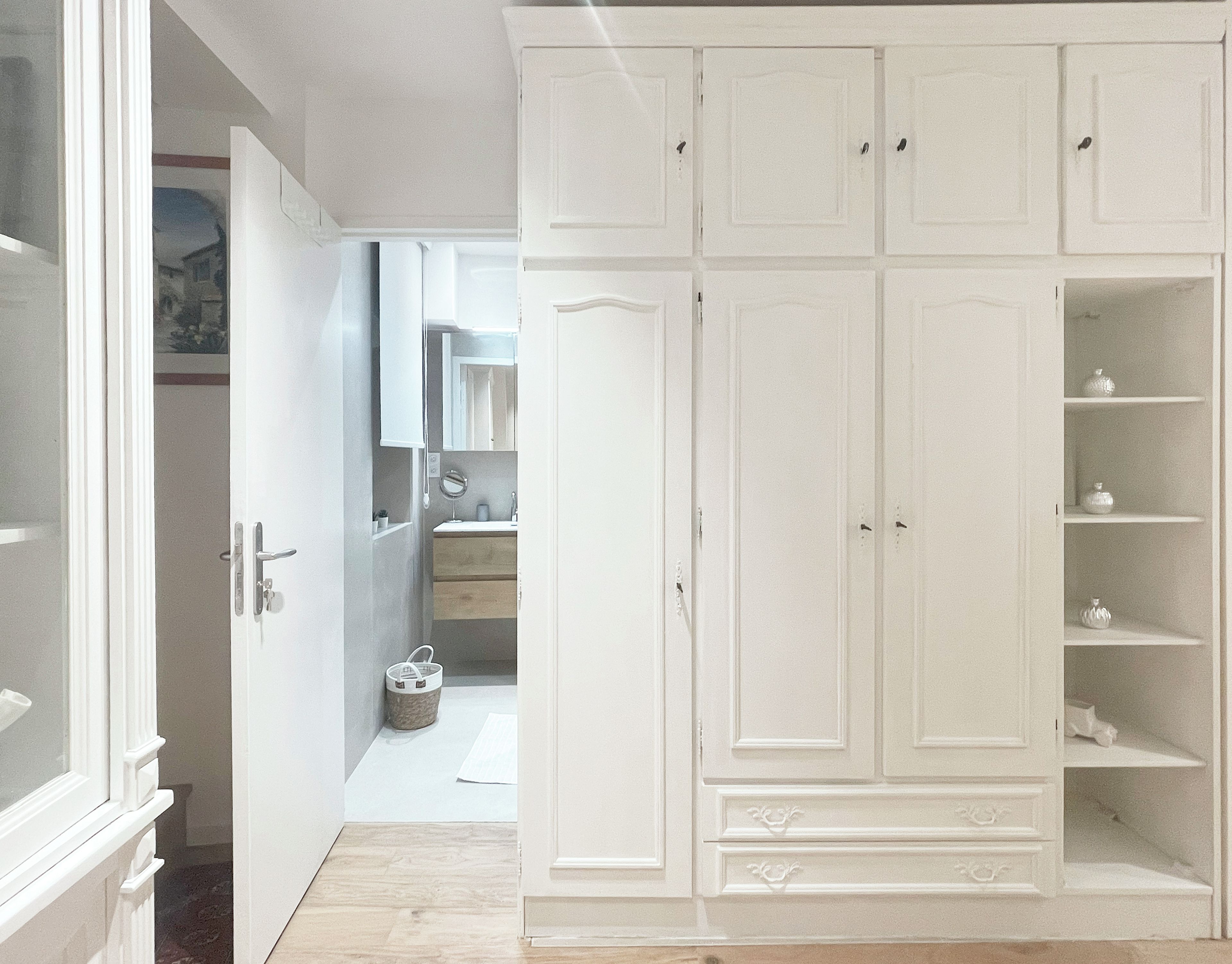 Una habitación con un armario grande de color blanco, piso de madera y una puerta que da a otra estancia.
