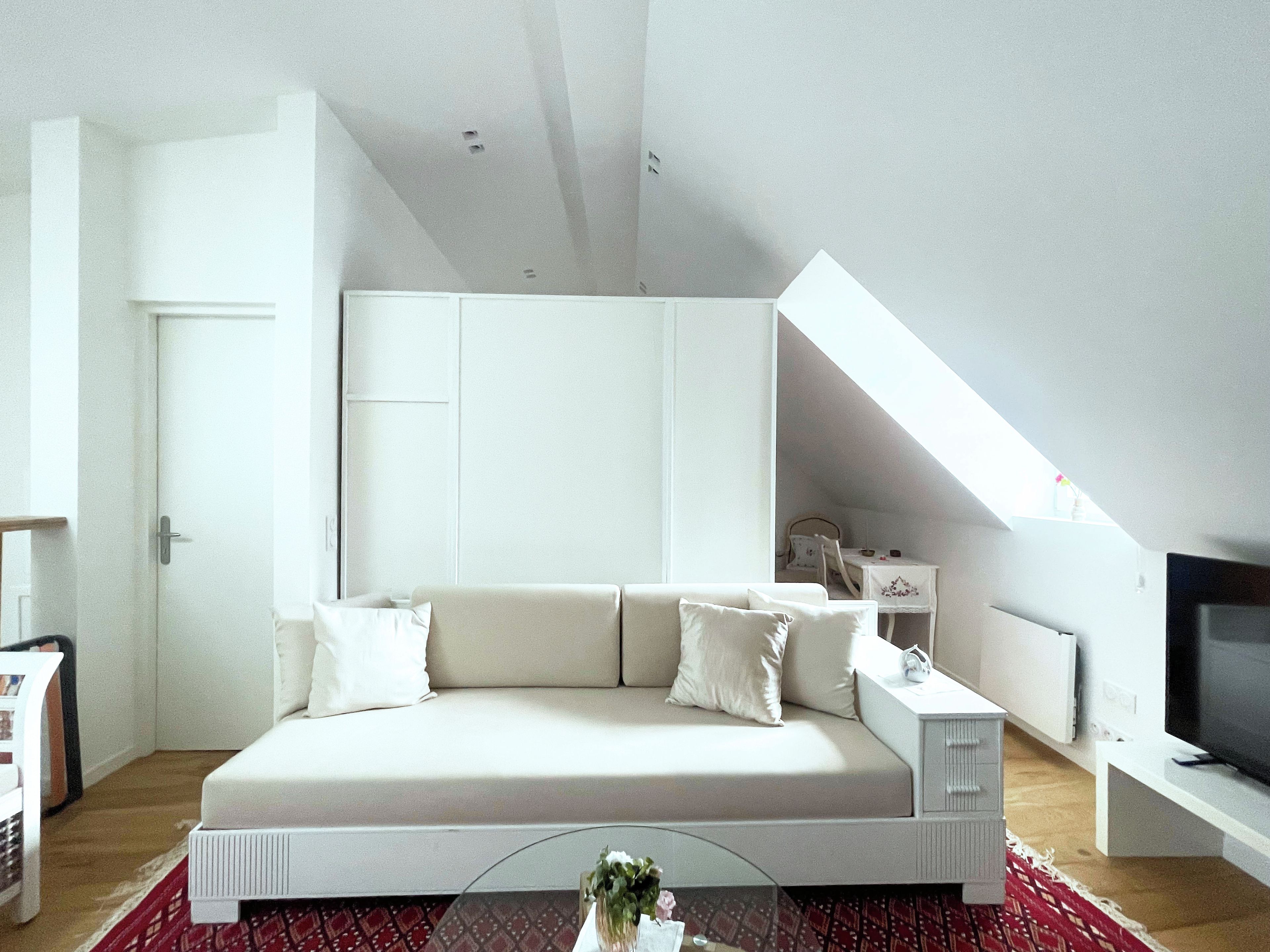 A modern, minimalist bedroom with a large bed, a television, and a skylight.