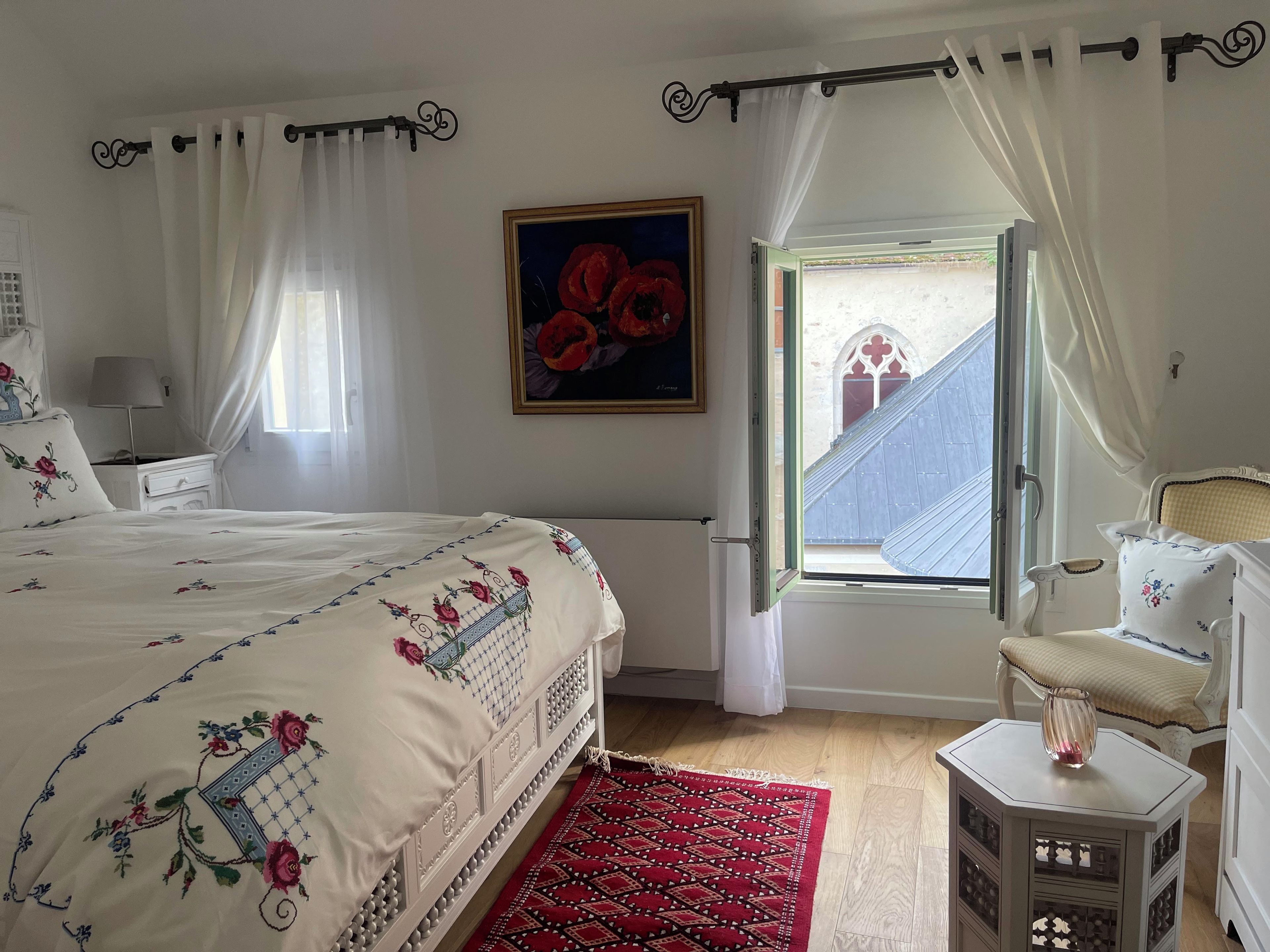 Quarto com cama, janela com cortinas, pintura e vista para um edifício.