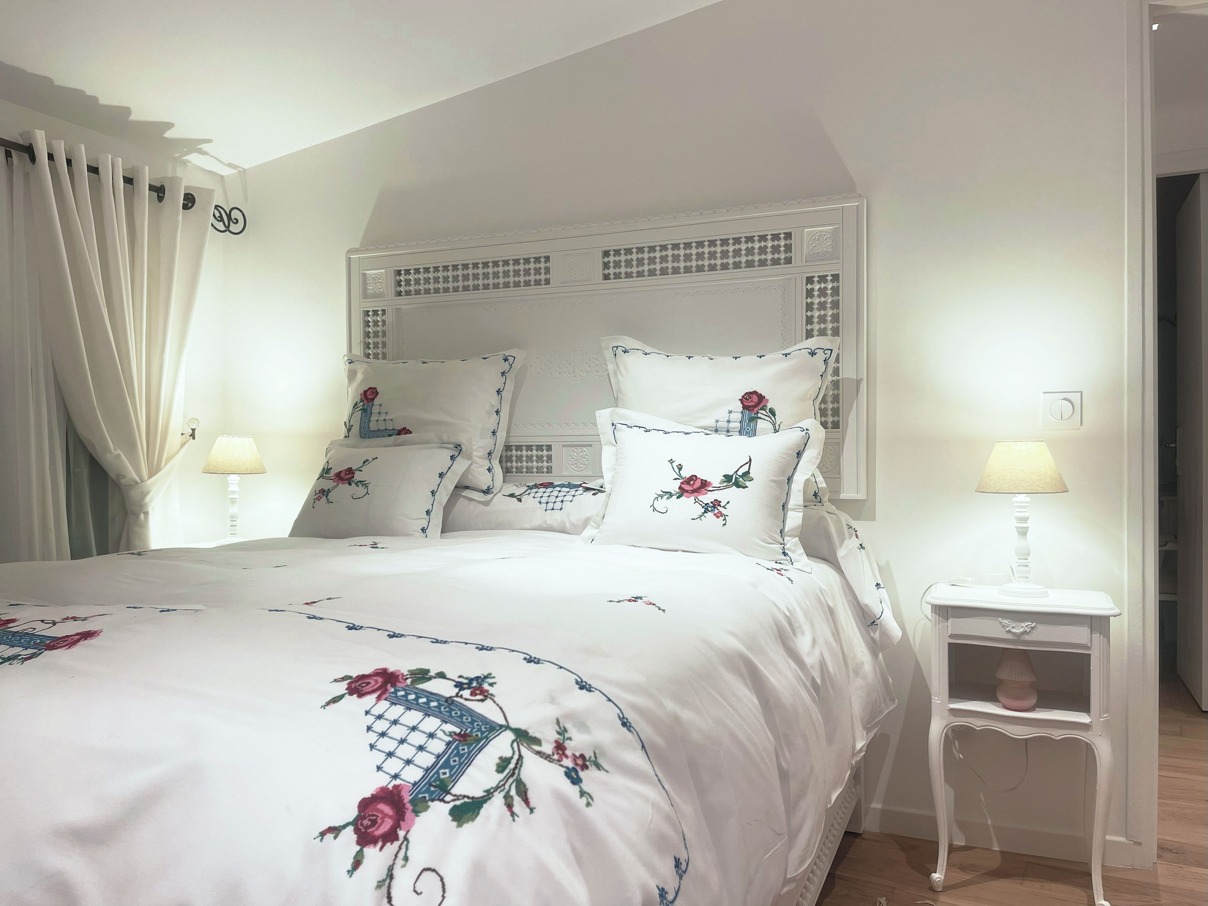 Une chambre à coucher avec un lit, des rideaux blancs, une table de chevet avec une lampe et une tête de lit décorative.