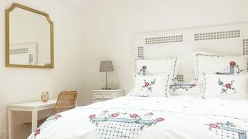Een slaapkamer met een bed, nachtkastje, lamp, stoel en spiegel.