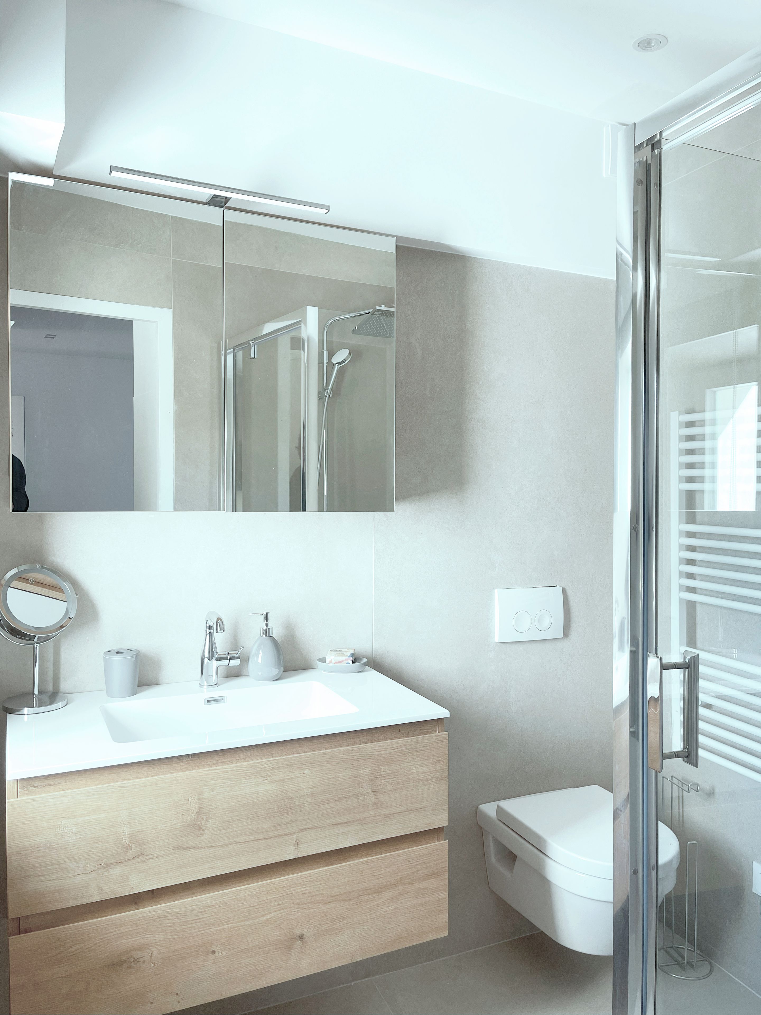 Un baño moderno con cabina de ducha de vidrio, un lavamanos blanco con espejo y un inodoro.