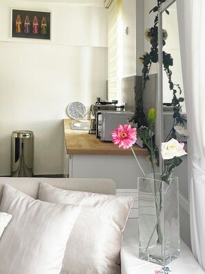 A modern room with a bed, a desk with a computer, a coffee machine, and a vase with flowers.
