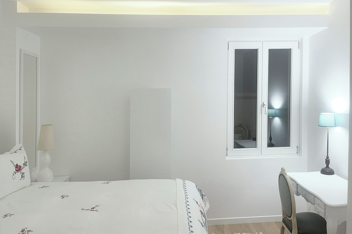 A bedroom with a bed, a desk, a chair, a window, and a wardrobe.