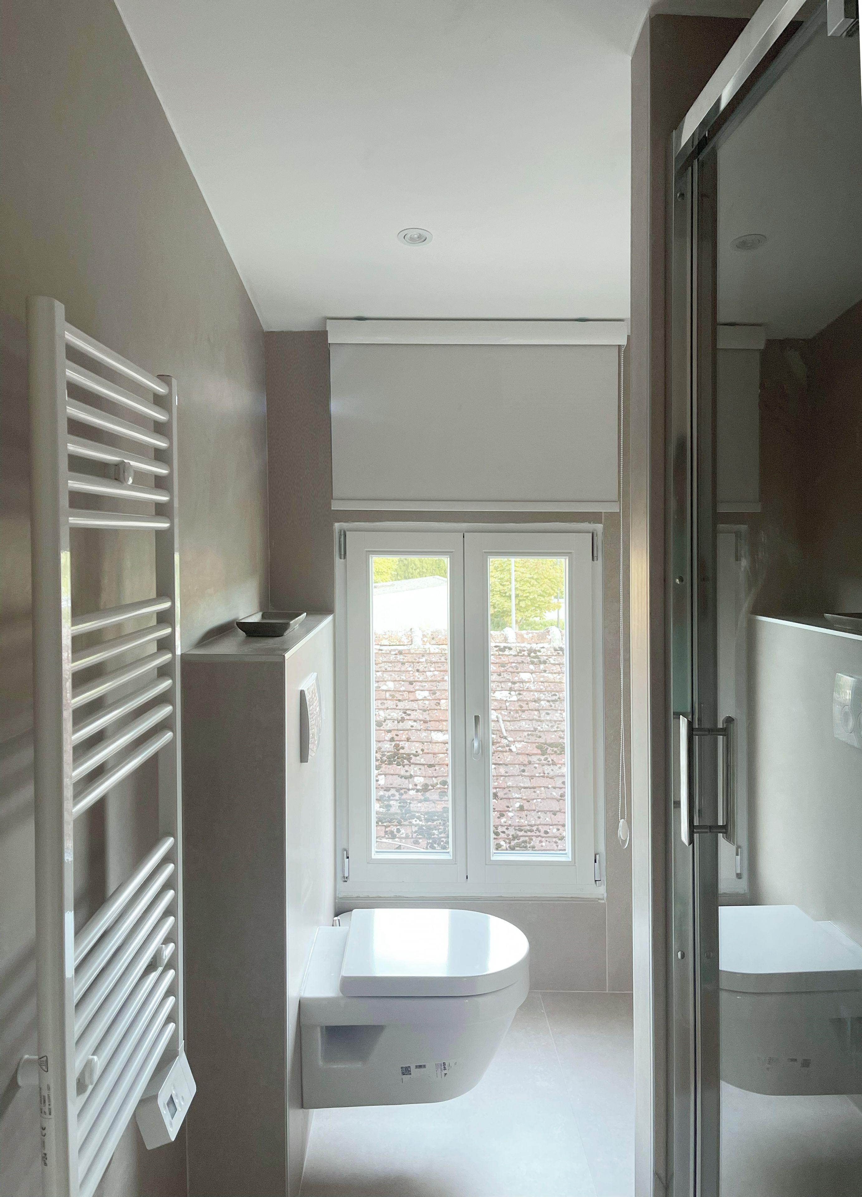 Ein modernes Badezimmer mit Toilette, Duschbereich und einem Fenster für natürliches Licht.