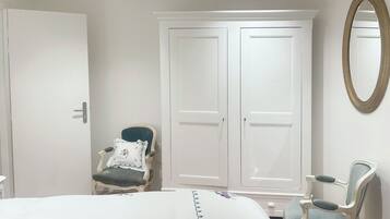 A bedroom with a bed, two chairs, a wardrobe, and a mirror.