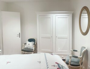 A bedroom with a bed, two chairs, a wardrobe, and a mirror.