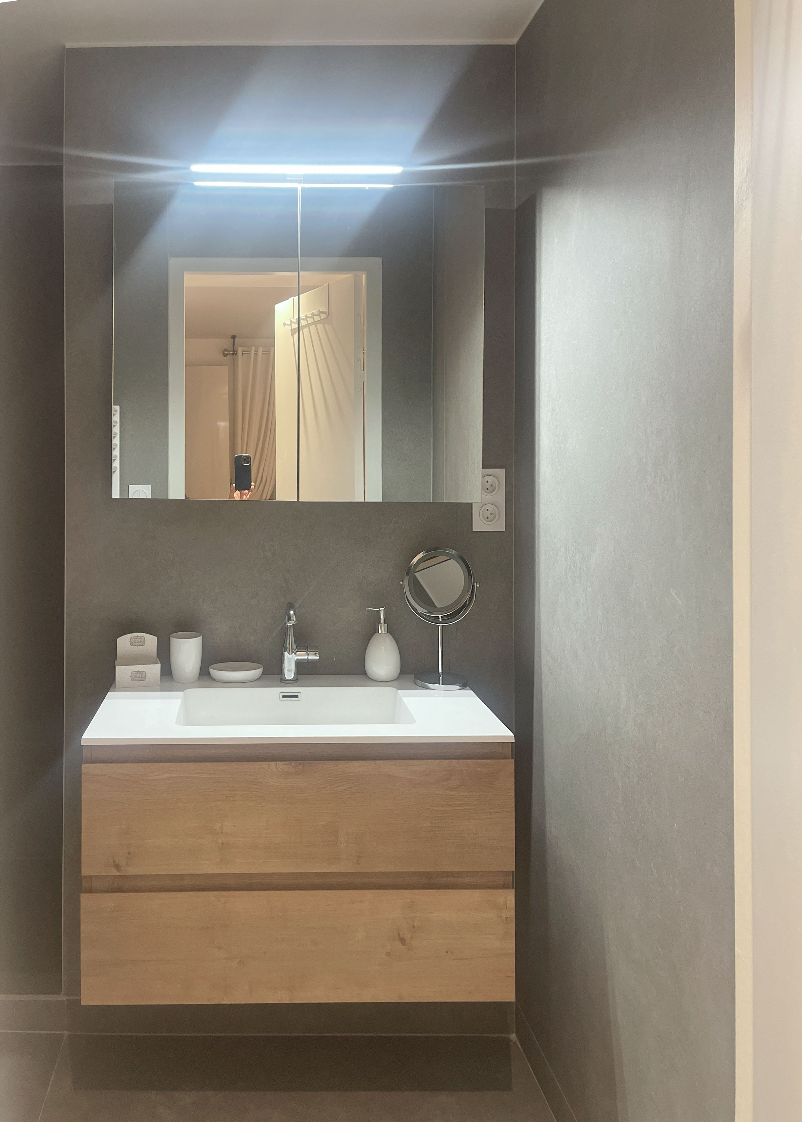 A modern bathroom with a white sink, wooden vanity, and a mirror above it.