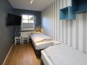 A bedroom with a bed, a TV, a window, and a striped wall. - Kiek Ut 9, Holiday Apartment 3 (Wyk auf Foehr)