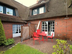 A brick house with a thatched roof, a wooden gate, and a patio with red chairs and a table. - Kiek Ut 9, Holiday Apartment 3 (Wyk auf Foehr)
