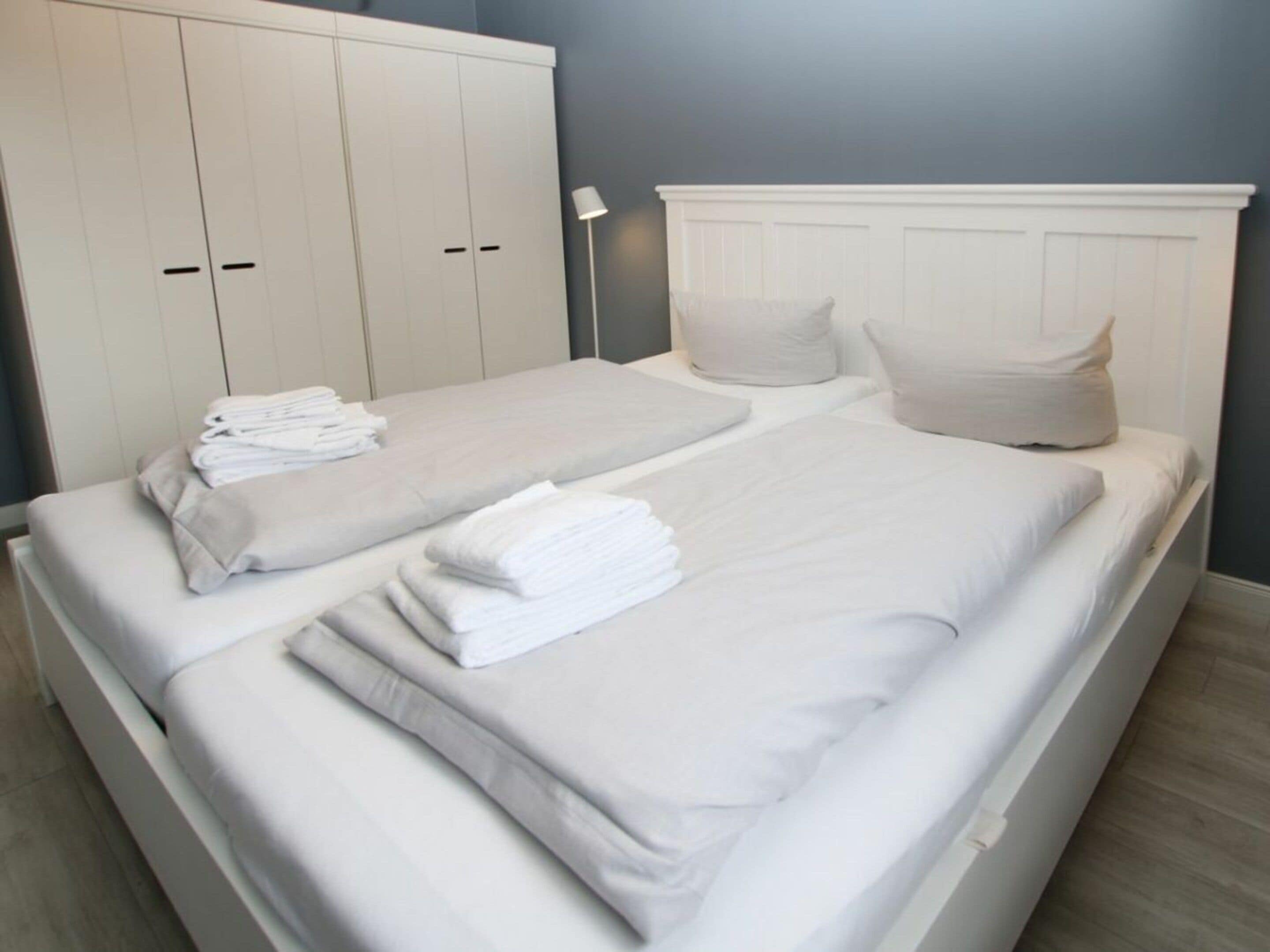 A double bed with white bedding and pillows, a nightstand with a lamp, and a wardrobe with two doors.