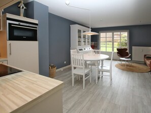 A modern kitchen with white cabinetry, a dining area with a round table and chairs, and a large window providing a view of the outdoors. - Kiek Ut 9, Holiday Apartment 3 (Wyk auf Foehr)
