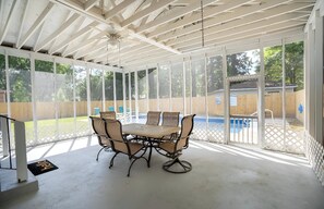 Eine überdachte Terrasse mit Tisch und Stühlen, im Hintergrund ein Pool und ein Holzzaun.