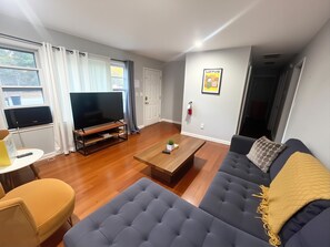Ein Wohnzimmer mit einer Couch, einem Couchtisch, einem Fernseher auf einem Schrank und einer Tür.