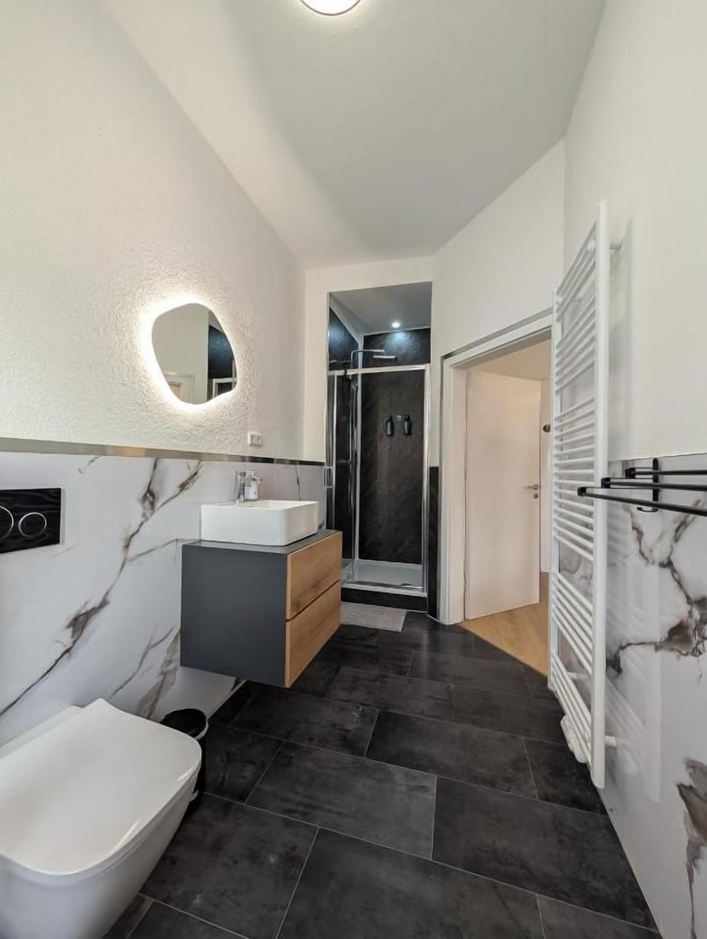 Ein modernes Badezimmer mit Toilette, Waschtisch mit Spiegel, Duschbereich und Handtuchhalter.