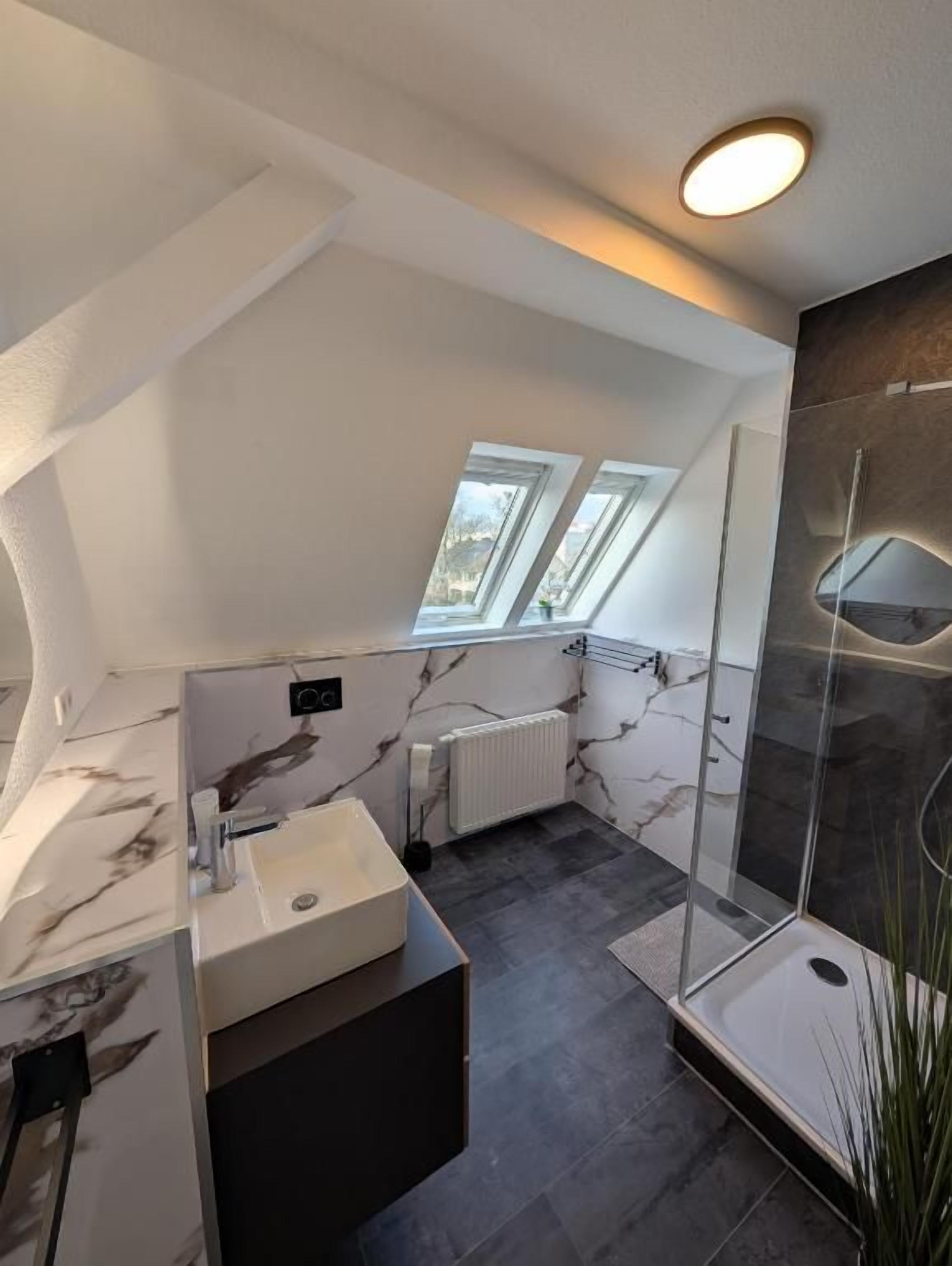 Ein modernes Badezimmer mit Dachfenster, einer Duschkabine aus Glas und einem мрамор-belagten Waschtisch.