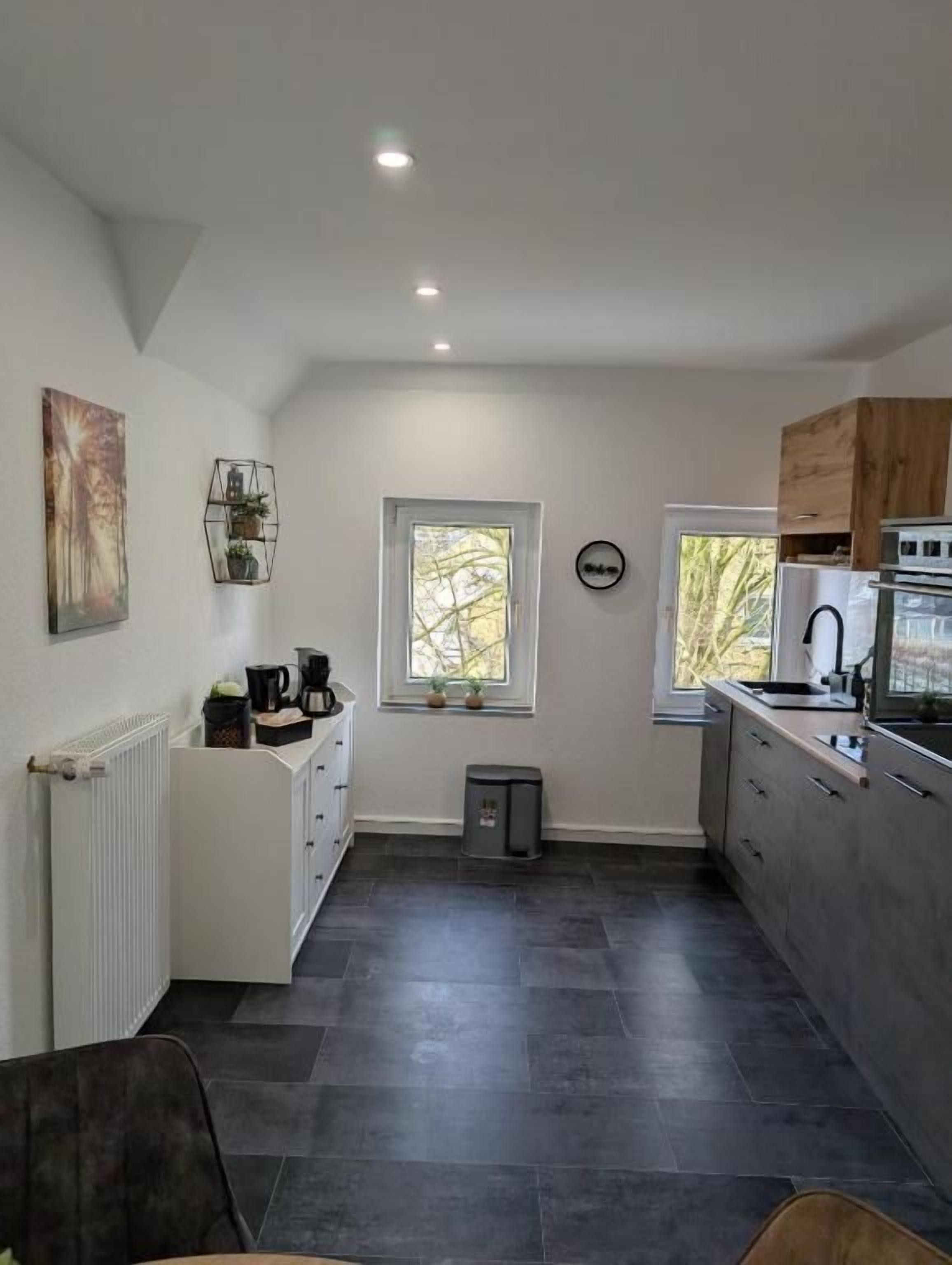 A modern kitchen with dark flooring, white cabinetry, and a window with a view of trees.