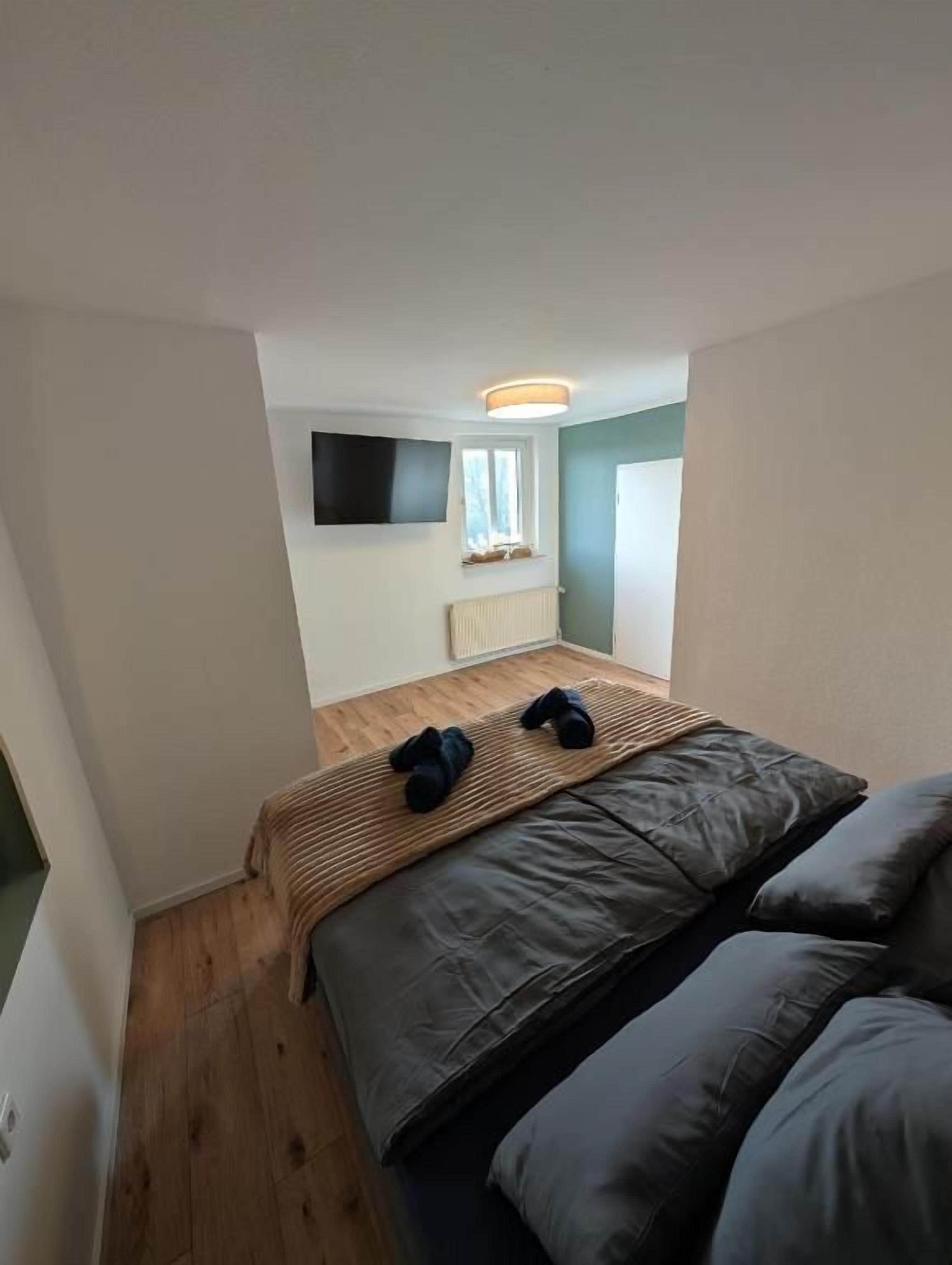 Ein kleiner, kompakter Raum mit einem Bett, einem an der Wand befestigten Flachbildfernseher und einem Fenster.