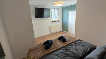 Ein kleiner, kompakter Raum mit einem Bett, einem an der Wand befestigten Flachbildfernseher und einem Fenster.