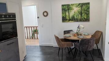 Eine moderne Küche mit dunklen Fliesen, ein Essbereich mit rundem Tisch und Stühlen und ein Wandbild mit Waldmotiv.