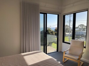 A bedroom with a bed, a chair, a large window, and a view of the outdoors. - Fisher St beach house Ventnor 150 metres to beach, veiws, spacious (Ventnor)