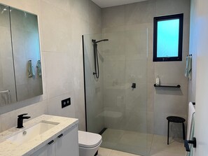 A modern bathroom with a glass shower enclosure, a white toilet, a sink with a marble countertop, and a mounted television. - Fisher St beach house Ventnor 150 metres to beach, veiws, spacious (Ventnor)