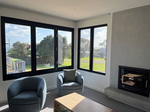 A modern living room with large windows, a fireplace, and two armchairs. - Fisher St beach house Ventnor 150 metres to beach, veiws, spacious (Ventnor)