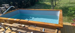 Una tina de madera rectangular con interior azul transparente, rodeada por una terraza con diversas herramientas y equipos.