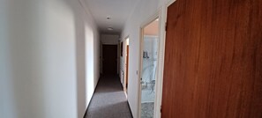 Un pasillo con piso alfombrado, paredes blancas y una puerta de madera a la derecha.
