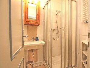 A bathroom with a glass-enclosed shower, a sink with a mirror above it, and a wooden cabinet. - Holiday Apartment in Fohr With 2 Bedrooms (Wyk auf Foehr)