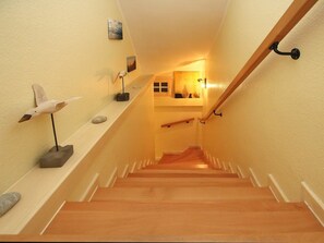 Un escalier en bois avec une rampe, des murs blancs et des objets décoratifs, notamment une sculpture d’oiseau et un vase.