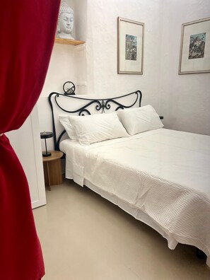 Ein Schlafzimmer mit einem Bett, einem Nachttisch, einer Wandablage mit einer Büste und zwei gerahmten Bildern.