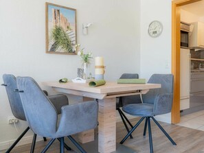 Un coin repas avec une table en bois, quatre chaises grises, une horloge et un tableau encadré au mur.