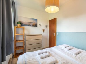 A bedroom with a bed, a wooden shelf with a plant, a painting on the wall, and a door. - 1 in the Westmarken Building (St. Peter-Ording)