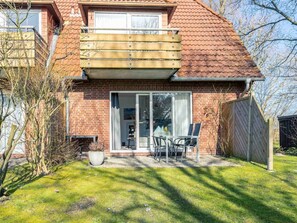 A two-story house with a red-tiled roof, a balcony, and a sliding glass door leading to a patio with a table and chairs. - 1 in the Westmarken Building (St. Peter-Ording)